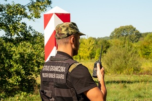 Funkcjonariusz SG będący przy znaku granicznym rozmawia przez radio słuzbowe